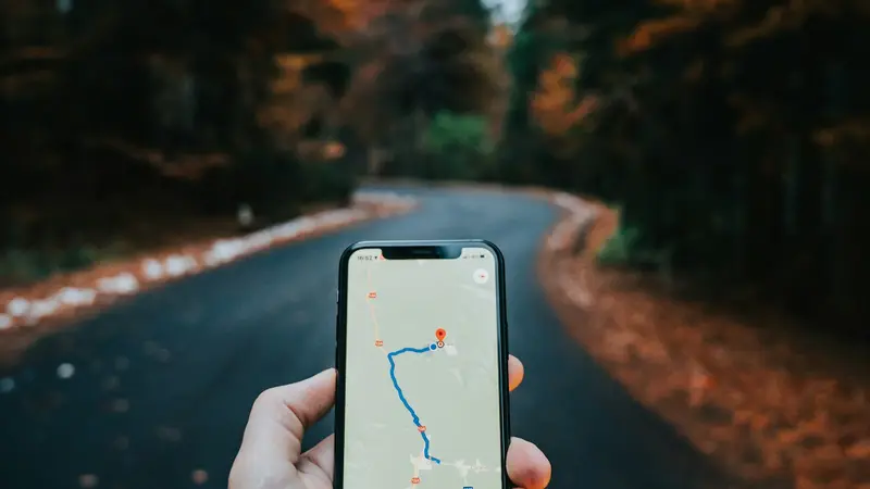 Mão segurando um celular com uma rota traçada no mapa, em uma estrada