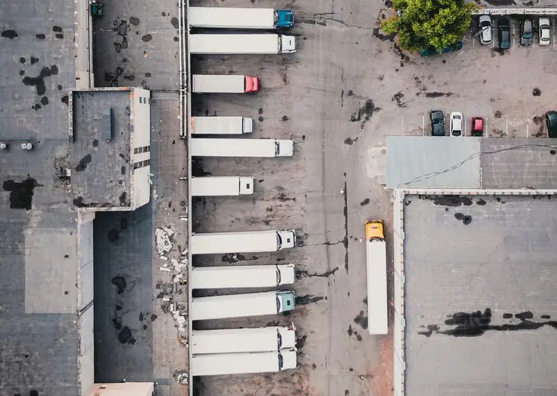 Vista aérea de caminhões estacionados lado a lado nas docas de um galpão logístico